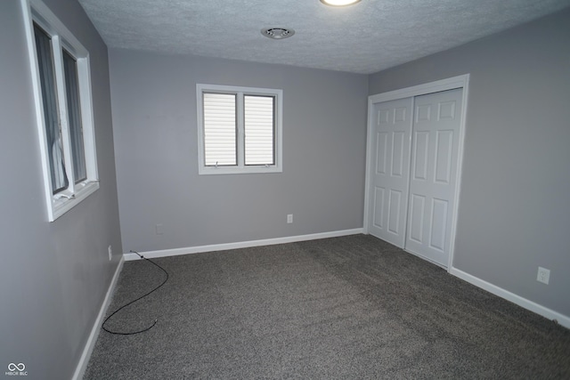 unfurnished bedroom featuring dark carpet, a textured ceiling, and baseboards