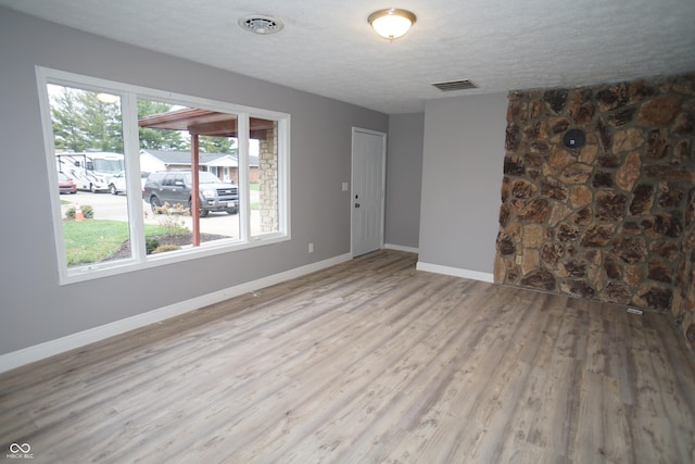 spare room with visible vents, a textured ceiling, baseboards, and wood finished floors