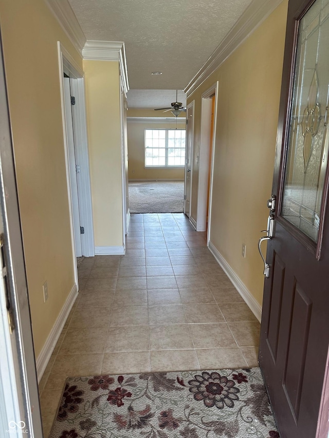 hallway featuring ornamental molding, a textured ceiling, baseboards, and light tile patterned floors