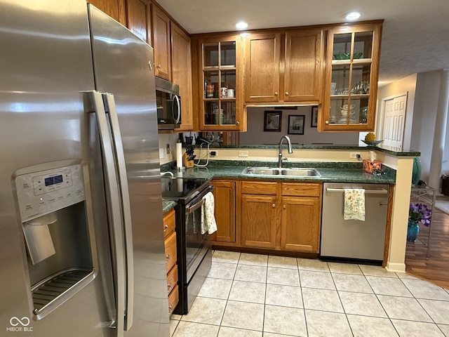 kitchen with appliances with stainless steel finishes, dark countertops, brown cabinetry, and a sink