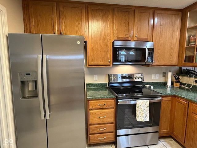 kitchen with light tile patterned floors, appliances with stainless steel finishes, brown cabinetry, and glass insert cabinets