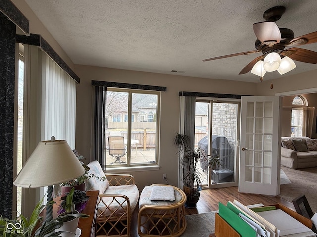 living area featuring french doors, visible vents, a ceiling fan, a textured ceiling, and wood finished floors