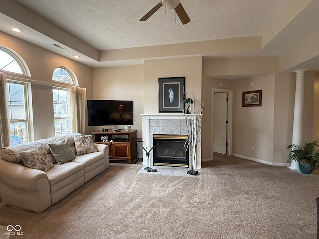 living area featuring carpet flooring, visible vents, baseboards, a tiled fireplace, and decorative columns