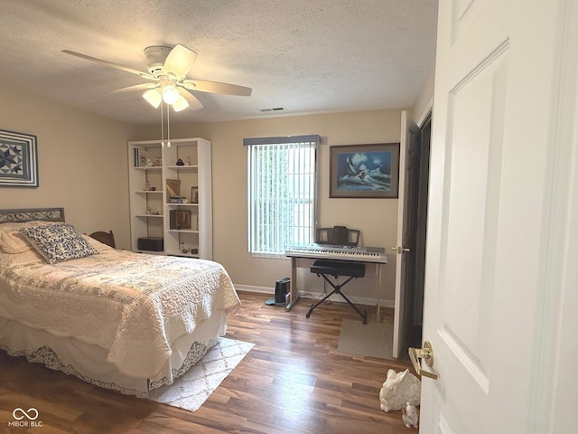 bedroom featuring baseboards, visible vents, a ceiling fan, wood finished floors, and a textured ceiling