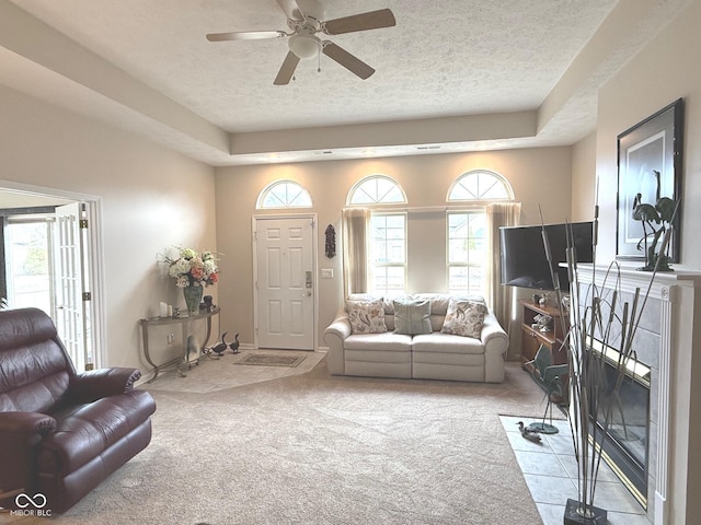 living room featuring light carpet, ceiling fan, a tiled fireplace, and a textured ceiling