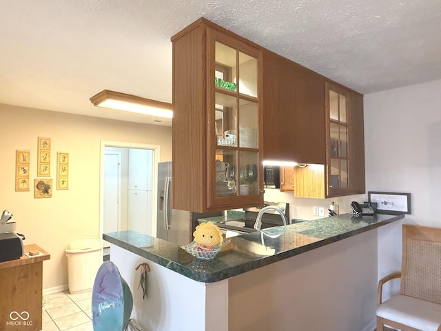 kitchen featuring a peninsula, light tile patterned floors, stainless steel fridge, and glass insert cabinets