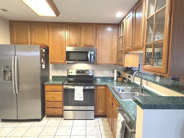 kitchen featuring stainless steel appliances, dark countertops, brown cabinetry, and a sink