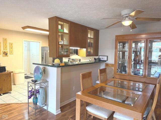 kitchen featuring a textured ceiling, light wood-style floors, appliances with stainless steel finishes, dark countertops, and glass insert cabinets