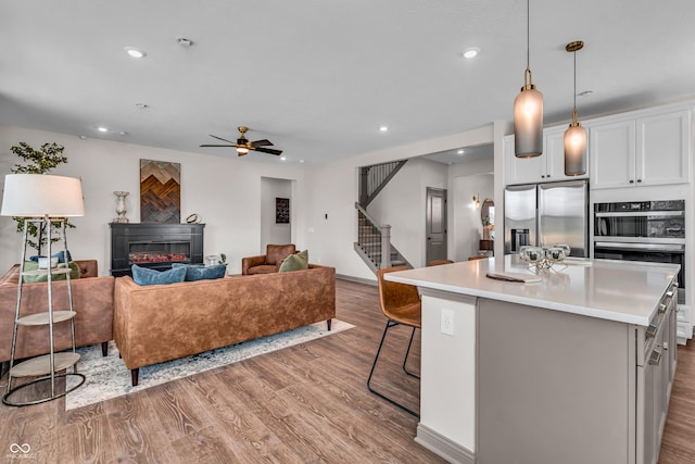 kitchen featuring a kitchen island, a glass covered fireplace, wood finished floors, stainless steel appliances, and light countertops