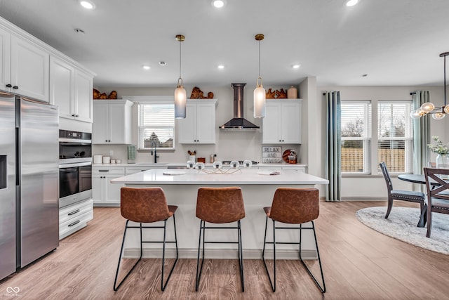 kitchen featuring light countertops, wall chimney range hood, appliances with stainless steel finishes, and a center island