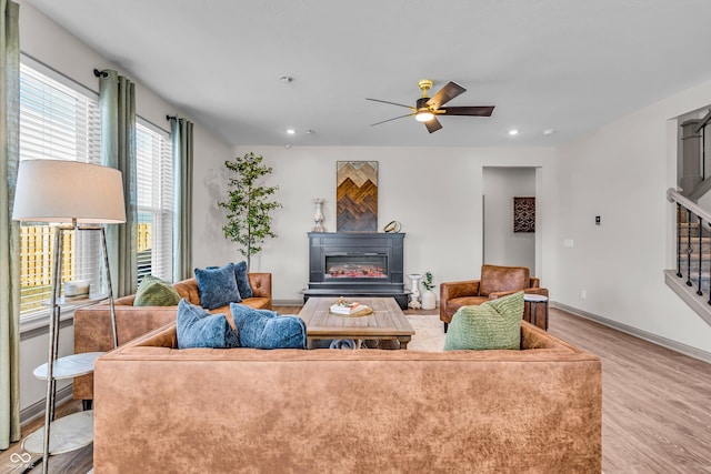 living room featuring a glass covered fireplace, recessed lighting, light wood finished floors, baseboards, and stairs