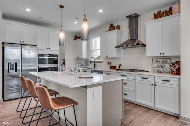 kitchen with stainless steel appliances, a kitchen bar, wall chimney exhaust hood, and white cabinetry