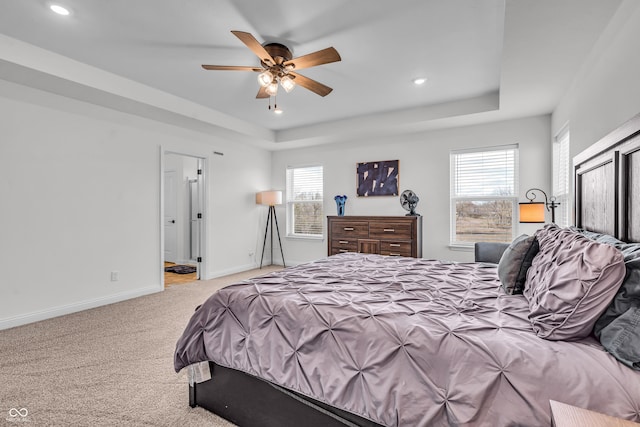 carpeted bedroom featuring a raised ceiling, multiple windows, and baseboards