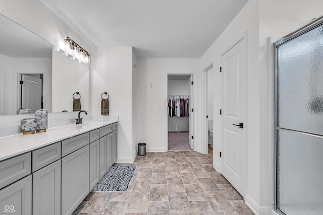 full bath featuring a shower stall, stone finish flooring, baseboards, toilet, and vanity