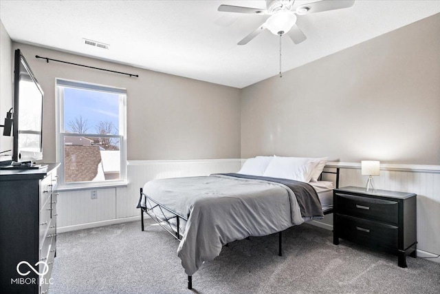 carpeted bedroom with visible vents, a ceiling fan, and wainscoting