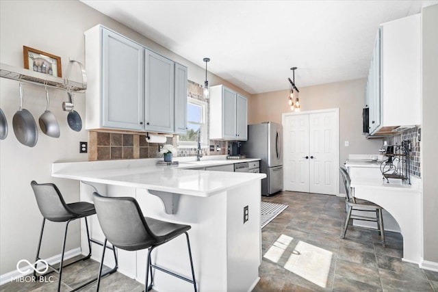 kitchen featuring a breakfast bar area, tasteful backsplash, light countertops, freestanding refrigerator, and a peninsula