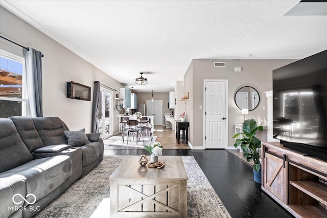 living room with dark wood-type flooring, visible vents, a textured ceiling, and baseboards