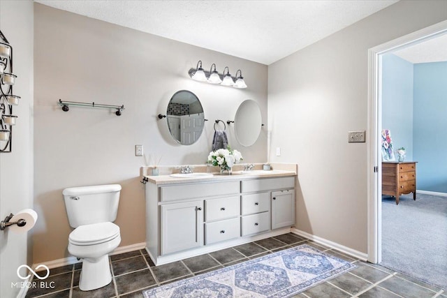 full bathroom with toilet, double vanity, baseboards, and a sink