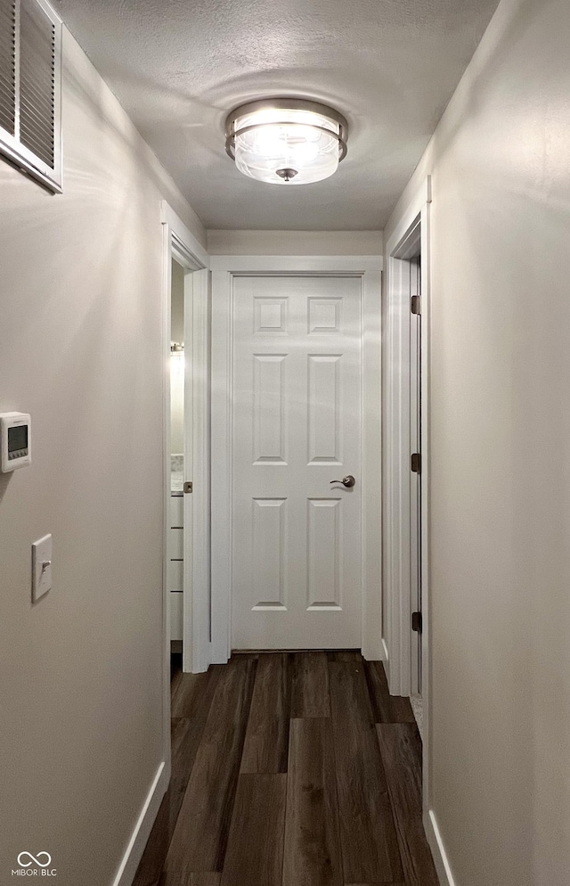 hall with baseboards, a textured ceiling, visible vents, and dark wood-type flooring