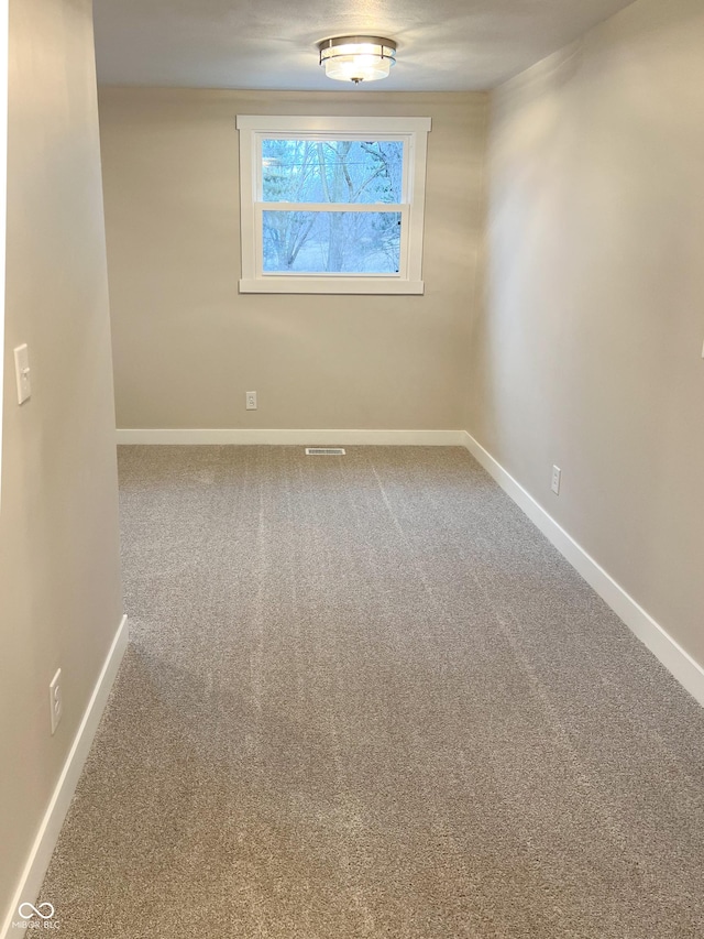 empty room with carpet flooring, visible vents, and baseboards