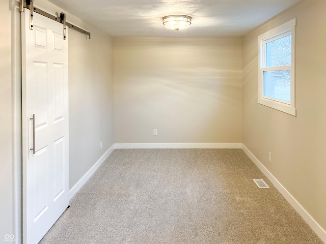 unfurnished room with carpet floors, visible vents, baseboards, and a barn door