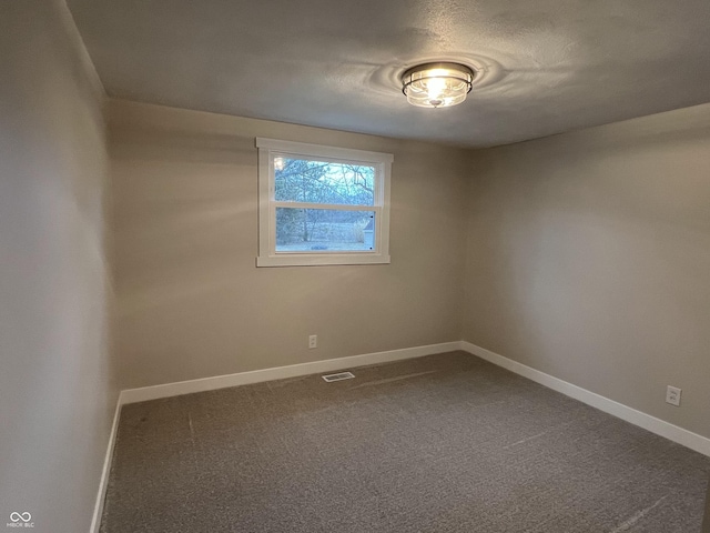 unfurnished room featuring dark colored carpet, visible vents, and baseboards