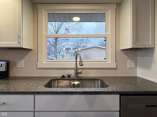 kitchen with dark stone countertops, white cabinetry, a sink, and dishwasher