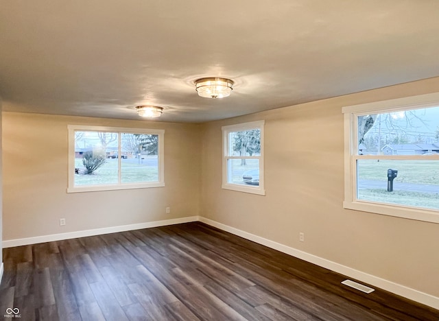 spare room with dark wood finished floors, visible vents, and baseboards