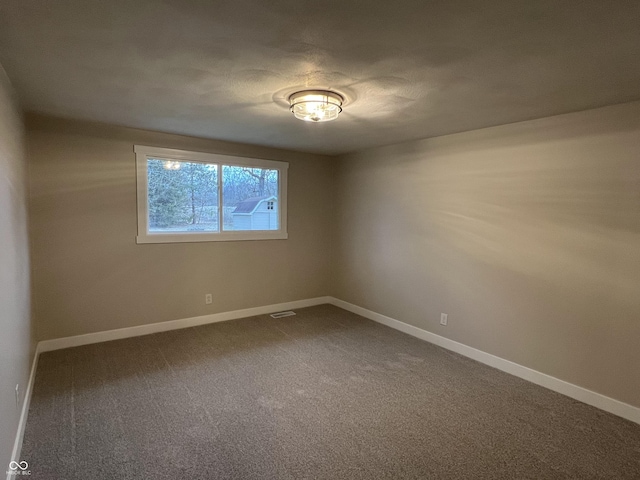 empty room with dark colored carpet, visible vents, and baseboards