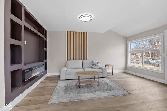 living room featuring light wood-type flooring, a glass covered fireplace, and baseboards