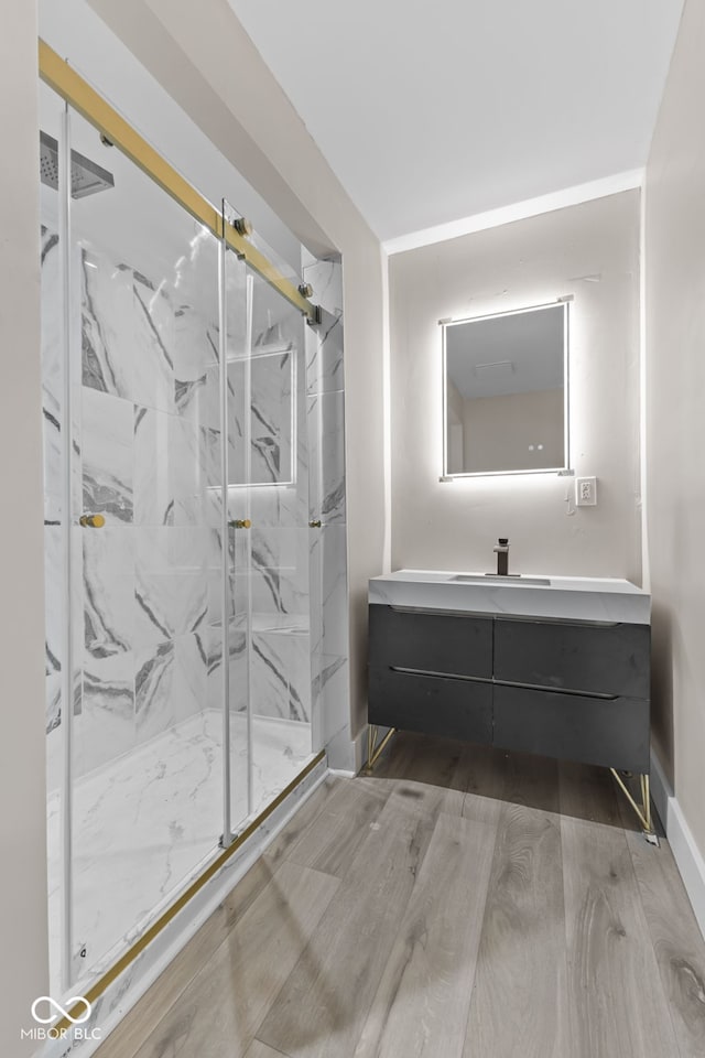 bathroom with baseboards, vanity, a marble finish shower, and wood finished floors