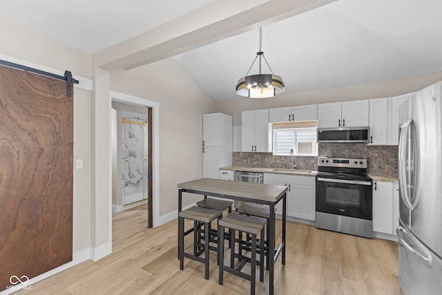 kitchen with stainless steel appliances, lofted ceiling, backsplash, a barn door, and a sink