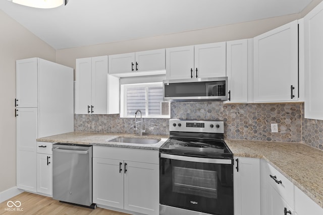 kitchen with tasteful backsplash, white cabinets, appliances with stainless steel finishes, light wood-type flooring, and a sink