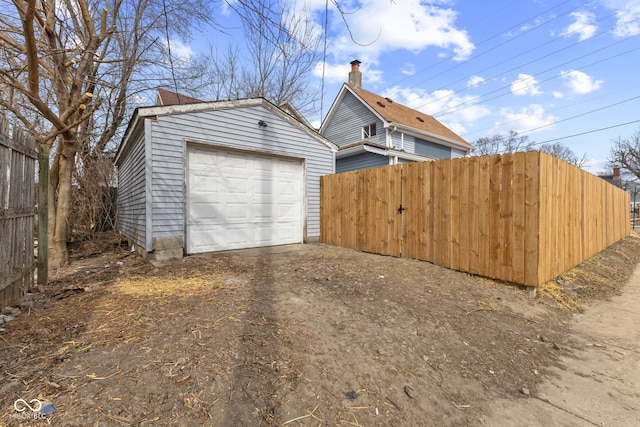 view of side of home featuring driveway, an outdoor structure, fence, and a detached garage