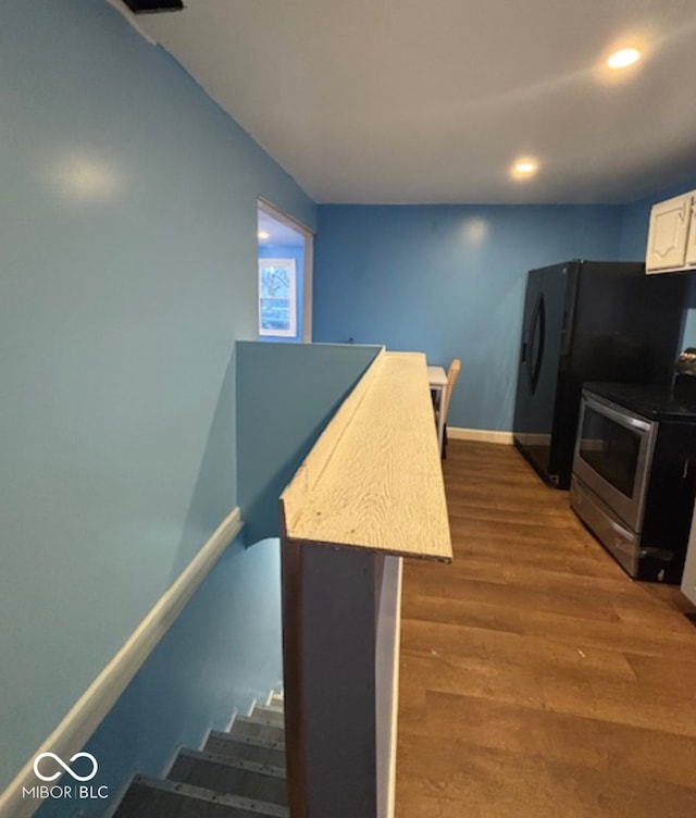 kitchen featuring baseboards, wood finished floors, freestanding refrigerator, stainless steel electric stove, and white cabinetry