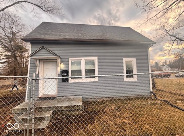 view of front of house featuring a shingled roof, fence, and a gate