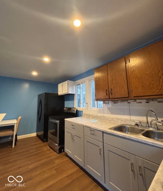 kitchen featuring stainless steel electric range oven, light countertops, dark wood-type flooring, a sink, and baseboards