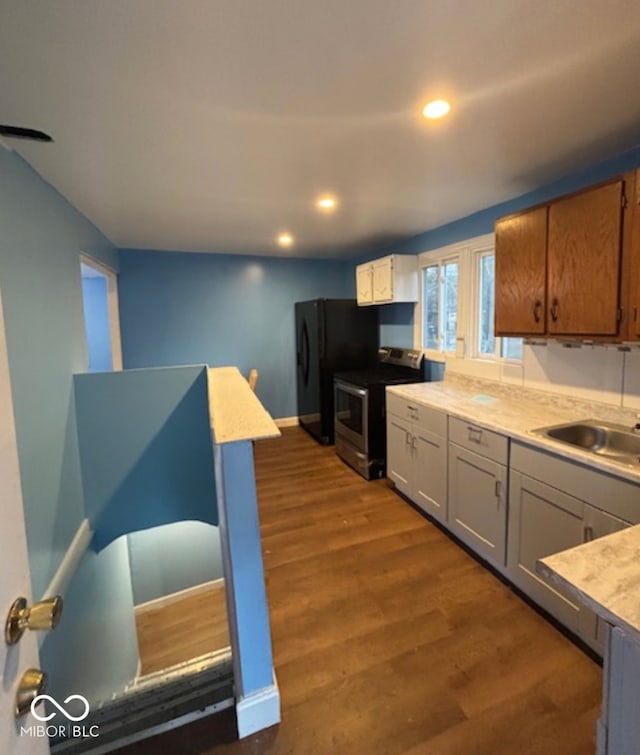 kitchen with dark wood finished floors, electric stove, freestanding refrigerator, light countertops, and a sink