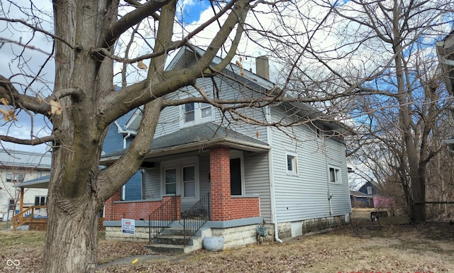 view of front of property with a shingled roof, a chimney, a porch, and brick siding