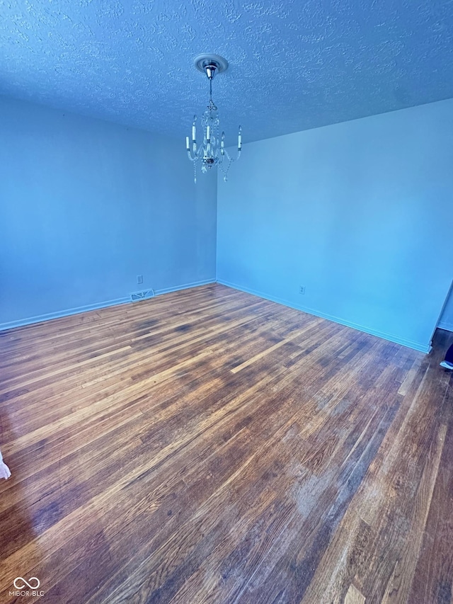 spare room with an inviting chandelier, a textured ceiling, baseboards, and wood finished floors