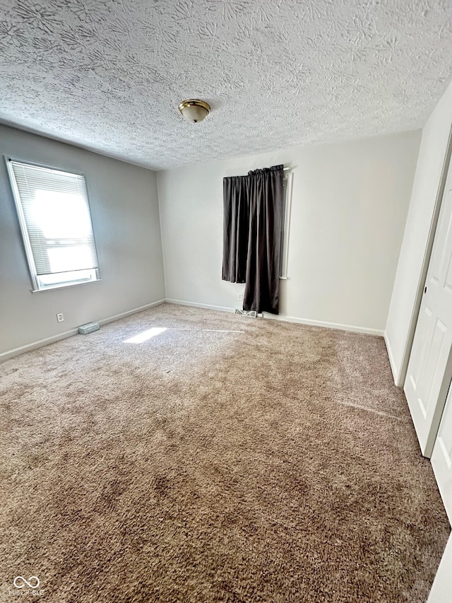 carpeted empty room featuring visible vents, a textured ceiling, and baseboards