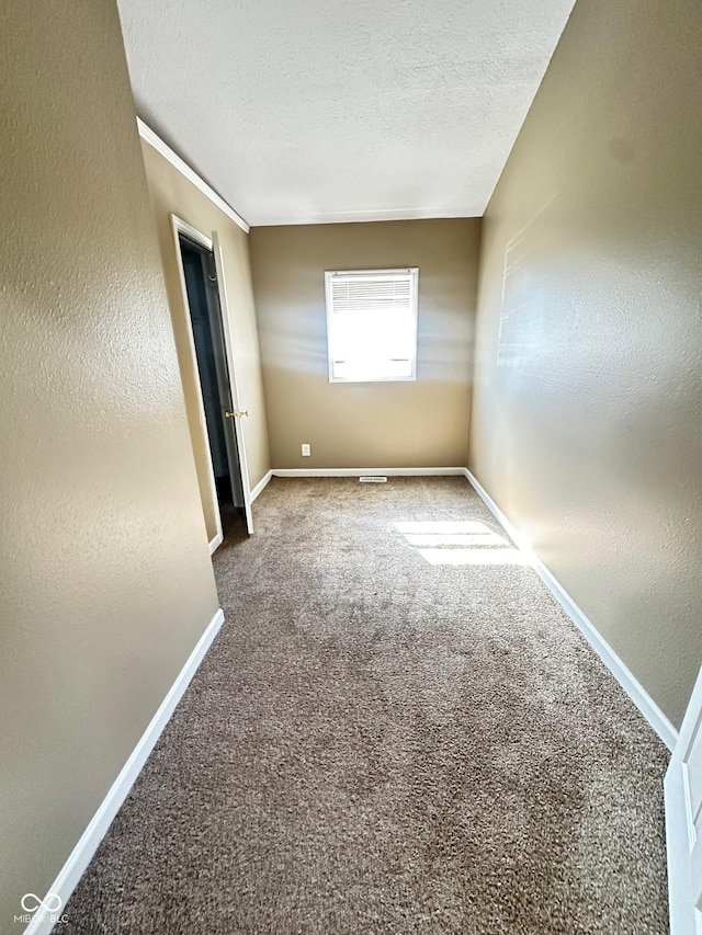 empty room with carpet flooring, a textured wall, a textured ceiling, and baseboards