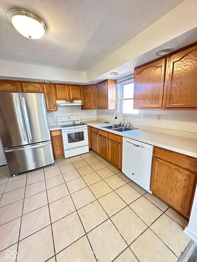 kitchen featuring light countertops, brown cabinetry, a sink, white appliances, and under cabinet range hood