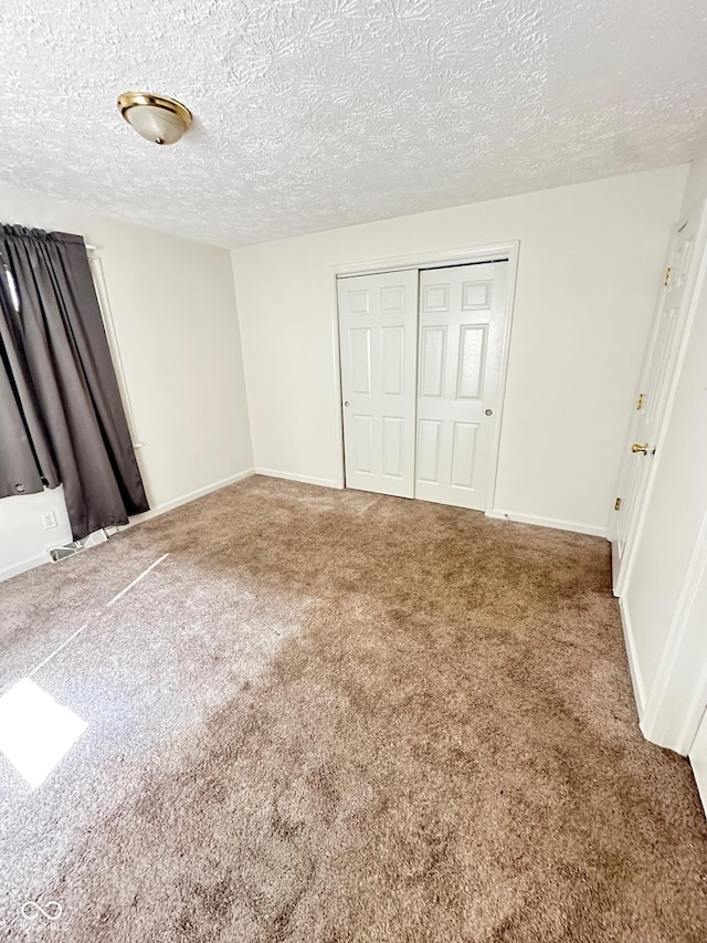 unfurnished bedroom with a textured ceiling, a closet, carpet flooring, and baseboards