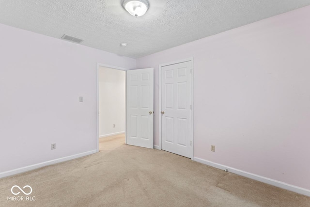 unfurnished bedroom with visible vents, light colored carpet, a textured ceiling, and baseboards