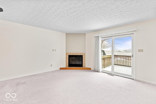 unfurnished living room with carpet, visible vents, baseboards, a tile fireplace, and a textured ceiling