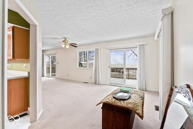 carpeted living room featuring a wealth of natural light, visible vents, baseboards, and a ceiling fan