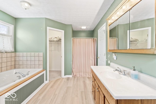 bathroom featuring a walk in closet, vanity, a garden tub, wood finished floors, and a textured ceiling