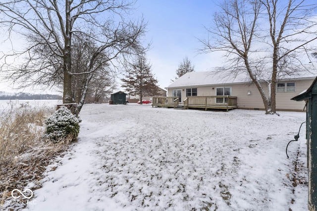 snow covered house with a deck, an outbuilding, and a storage unit