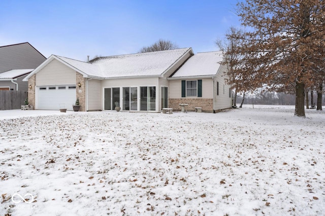 view of front facade with a sunroom, brick siding, an attached garage, and fence